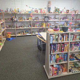 Overzicht van de winkelruimte met speelgoed en boeken op stellingen en een kastje met dvd's in het midden