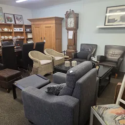 Zithoek met grijze stoelen, rieten fauteuils en bruine pouf in een kringloopwinkel