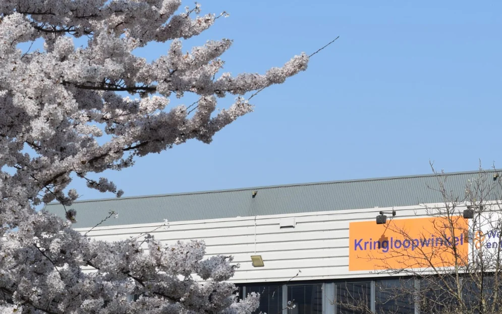 Exterieur van kringloopwinkel met wit en grijs golfplaten dak, oranje bord met winkelnaam, omgeven door besneeuwde bomen