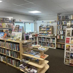 Winkelinterieur met boeken- en mediarekken, uitgestalde boeken op houten tafels, boekenkasten tegen de muren en decoratie aan