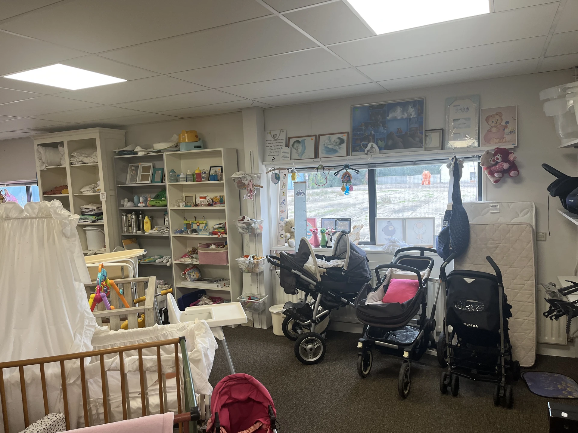 Winkelinterieur met kinderwagens, stellingen met spullen, ramen met uitzicht op straat