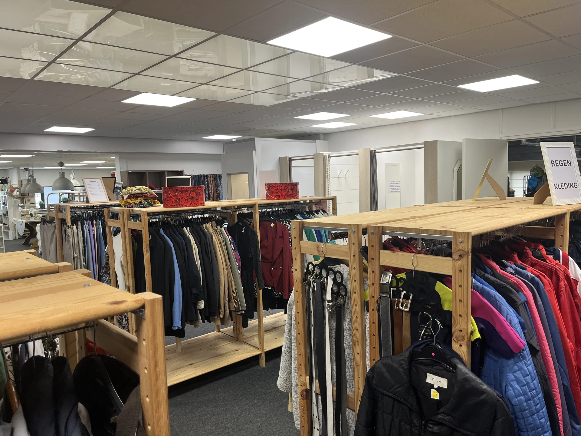 Winkelinterieur met houten rekken vol tweedehands kleding, onder het plafond met LED-panelen