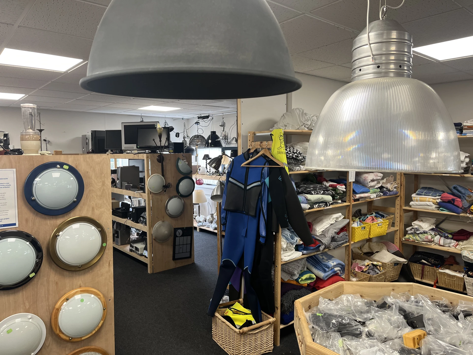Winkelinterieur met stellingen vol spullen, hanglampen en kledingrek met blauwe jassen