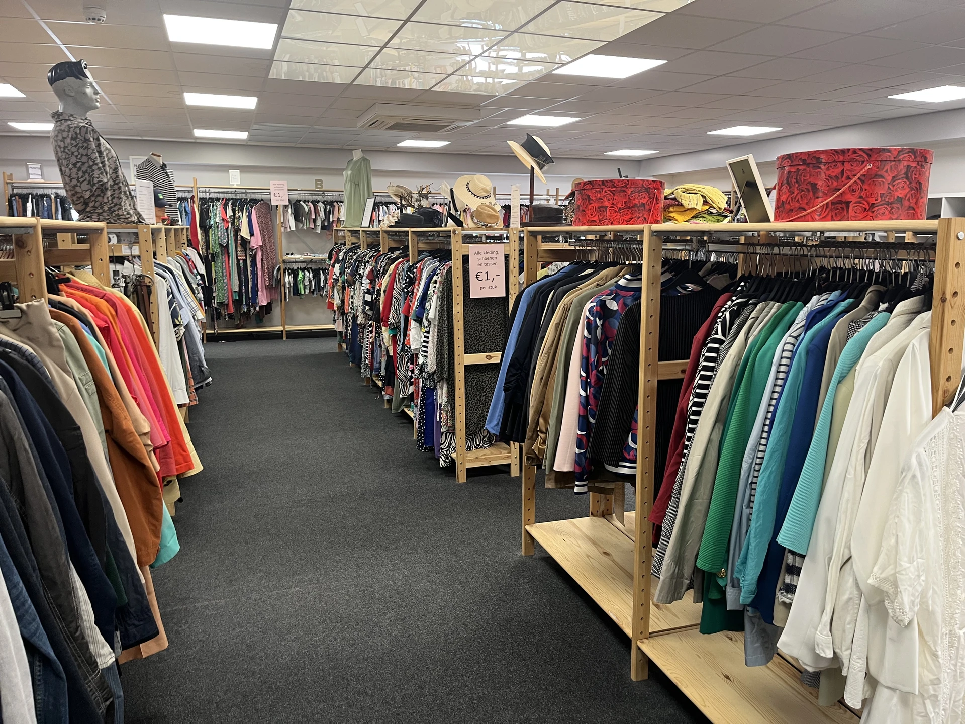 Winkelinterieur met houten kledingrekken vol tweedehands kleding in verschillende kleuren