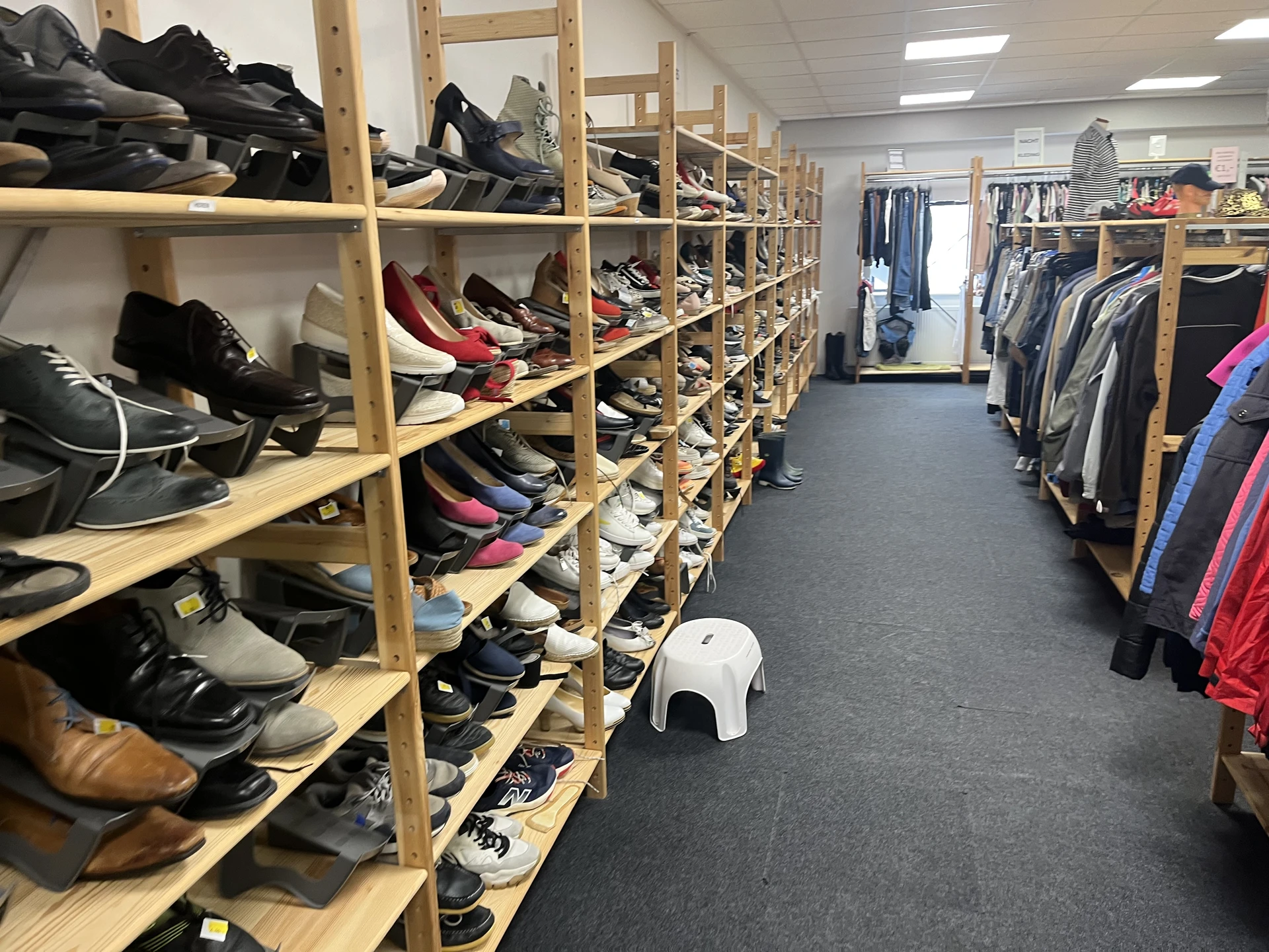 Houten stellingen met uitgestalde tweedehands schoenen en kleding aan rekken in kringloopwinkel