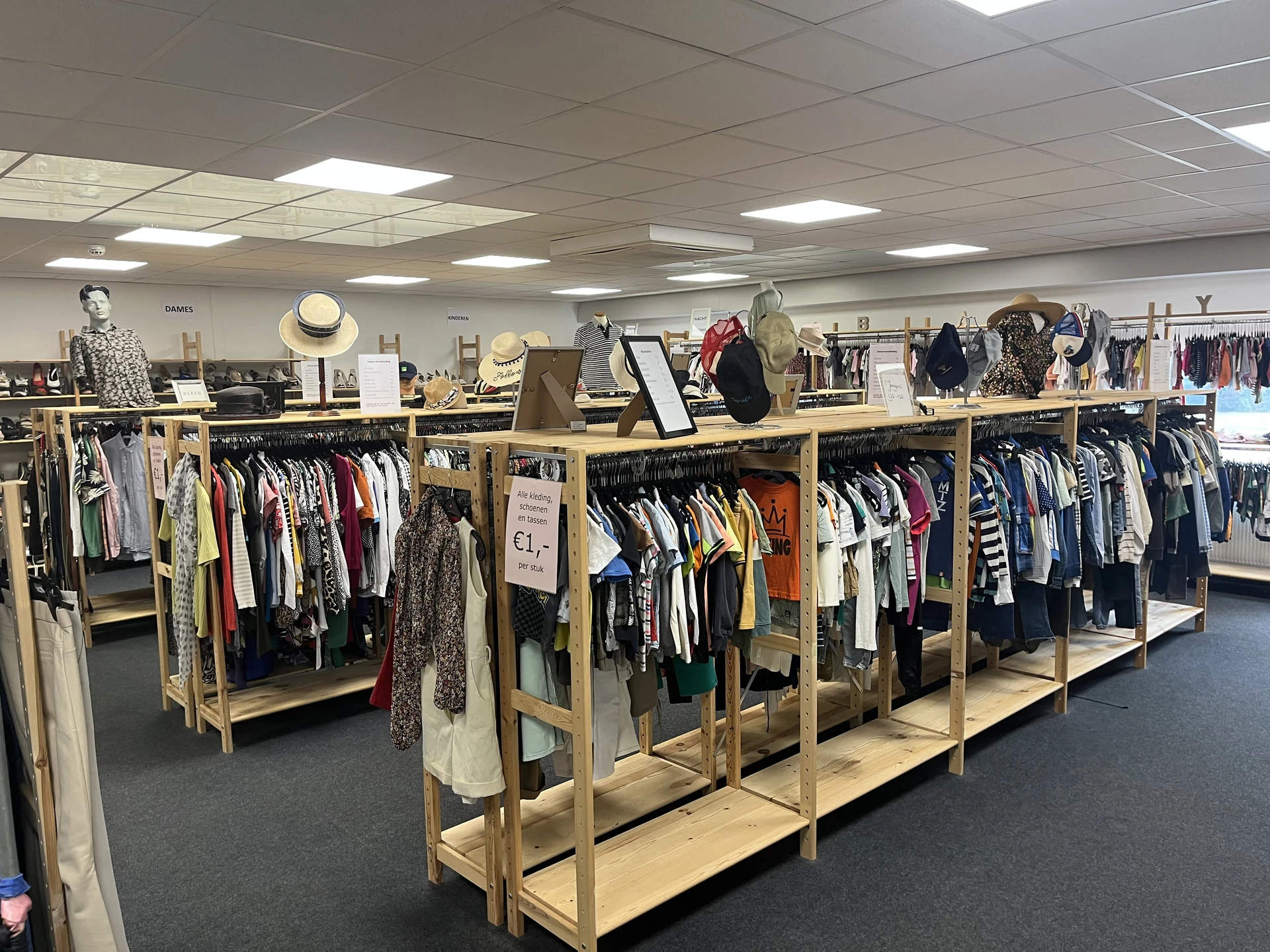 Winkelvloer met houten stellingen vol tweedehands kleding, uitgangspunt voor overzicht van kringloopwinkel