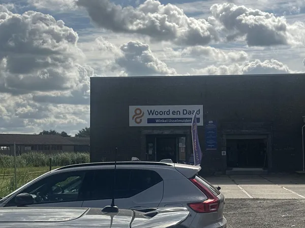Zwart pand van kringloopwinkel Woord en Daad met naam op gevel, auto op parkeerplaats