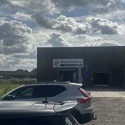 Zwart pand van kringloopwinkel Woord en Daad met naam op gevel, auto op parkeerplaats