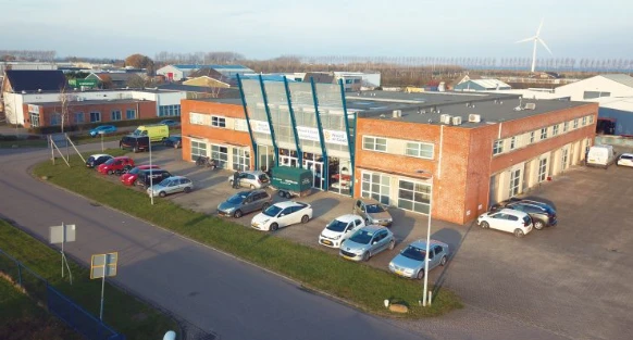 Exterieur van kringloopwinkel met oranje bakstenen gevel, groene luifels en parkeerplaats met auto's
