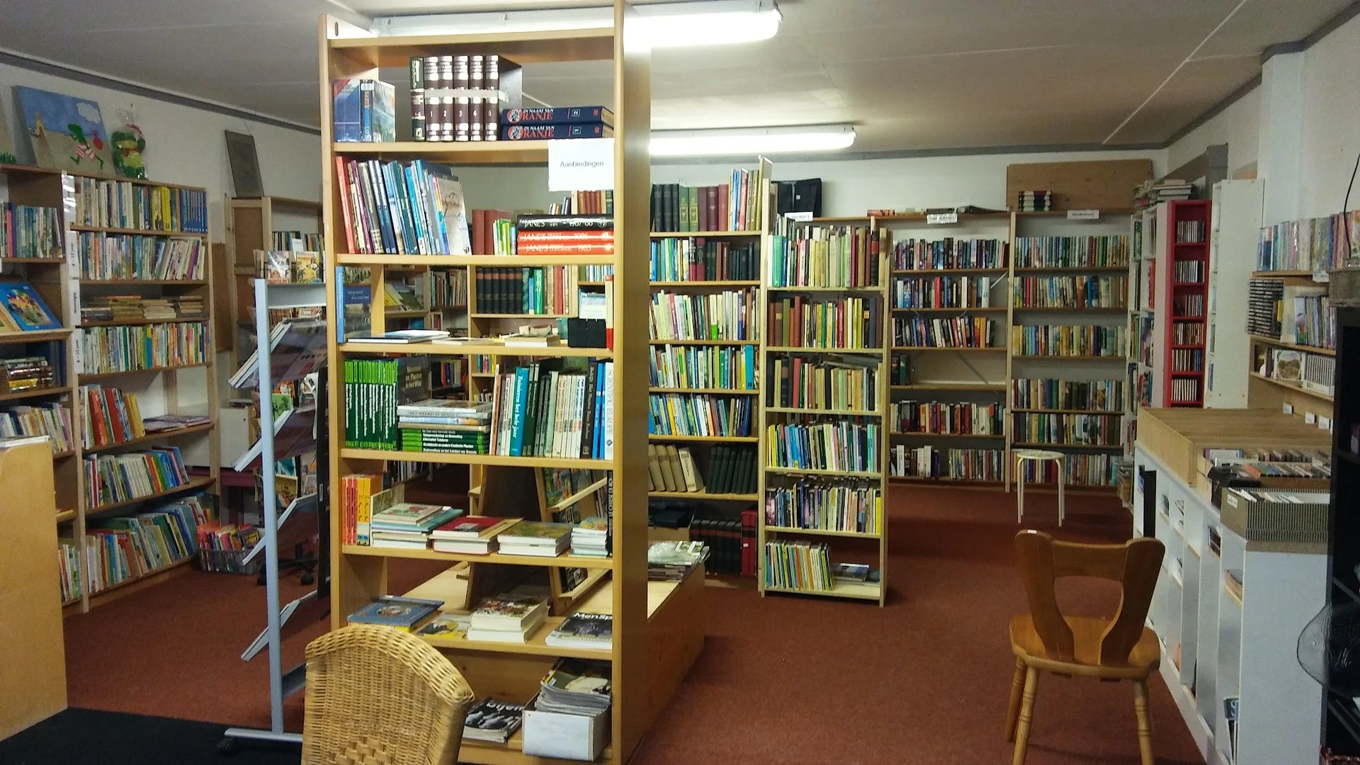 Boekenkasten en stellingen vol boeken in een kringloopwinkel, met houten meubels op een bruine vloer.