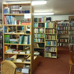 Boekenkasten en stellingen vol boeken in een kringloopwinkel, met houten meubels op een bruine vloer.