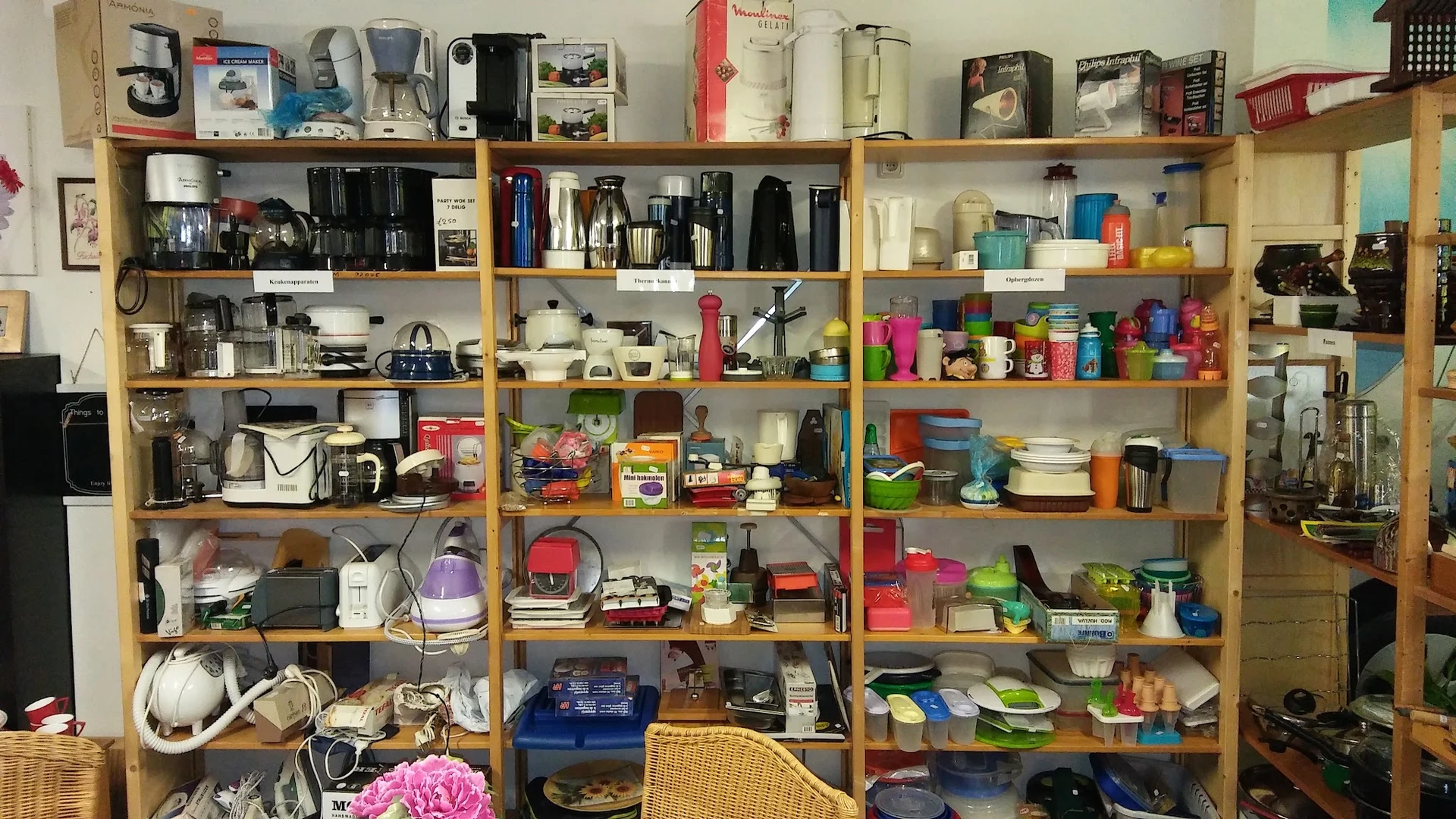 Houten stellingen vol met huishoudelijke artikelen, keukengerei, servies, opbergdozen en diverse gebruiksvoorwerpen