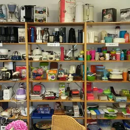 Houten stellingen vol met huishoudelijke artikelen, keukengerei, servies, opbergdozen en diverse gebruiksvoorwerpen