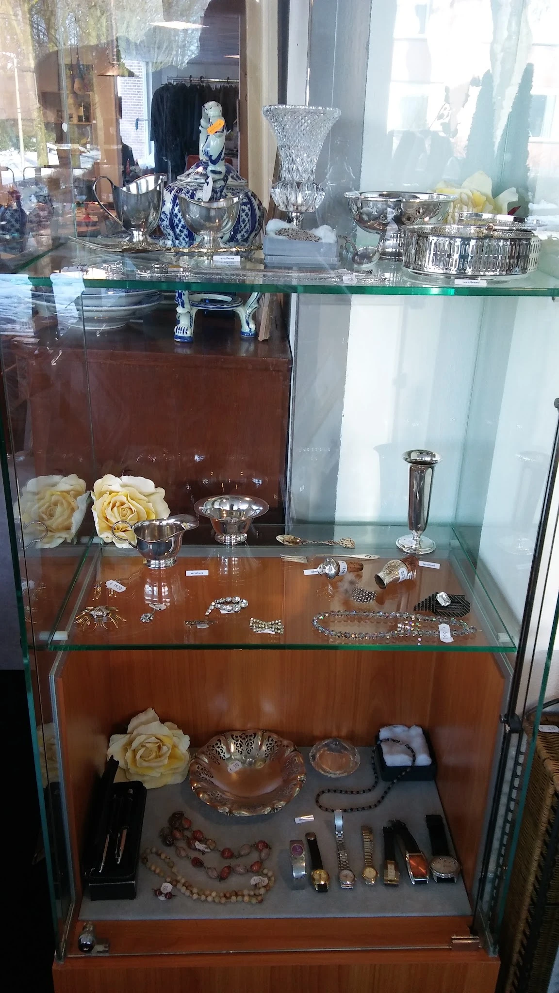 Glazen vitrinekast met sieraden, zilveren servies en decoratie-items op bruine achtergrond