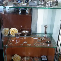 Glazen vitrinekast met sieraden, zilveren servies en decoratie-items op bruine achtergrond