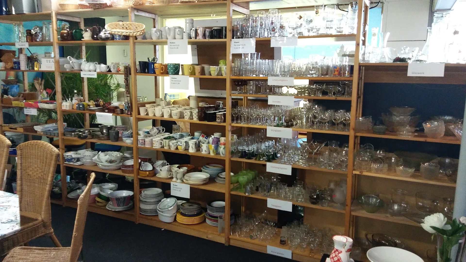 Houten stellingen vol met huishoudelijke artikelen: glazen, servies, pannen en decoratieve items in een kringloopwinkel