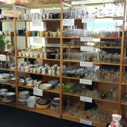Houten stellingen vol met huishoudelijke artikelen: glazen, servies, pannen en decoratieve items in een kringloopwinkel