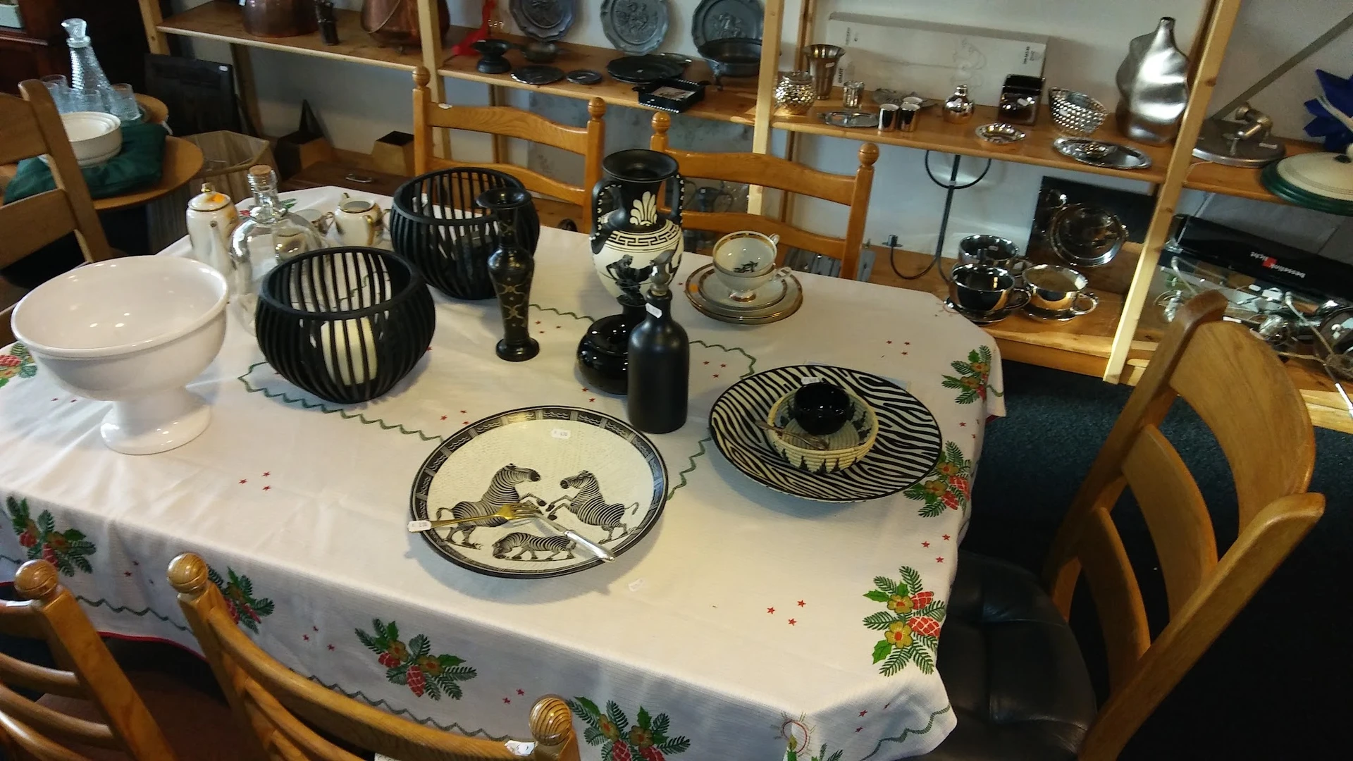 Tafel met decoratieve items: zwarte draadmanden, zwart beeld, decoratieve borden met vogelmotieven, zwarte kandelaars en ande