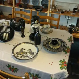 Tafel met decoratieve items: zwarte draadmanden, zwart beeld, decoratieve borden met vogelmotieven, zwarte kandelaars en ande