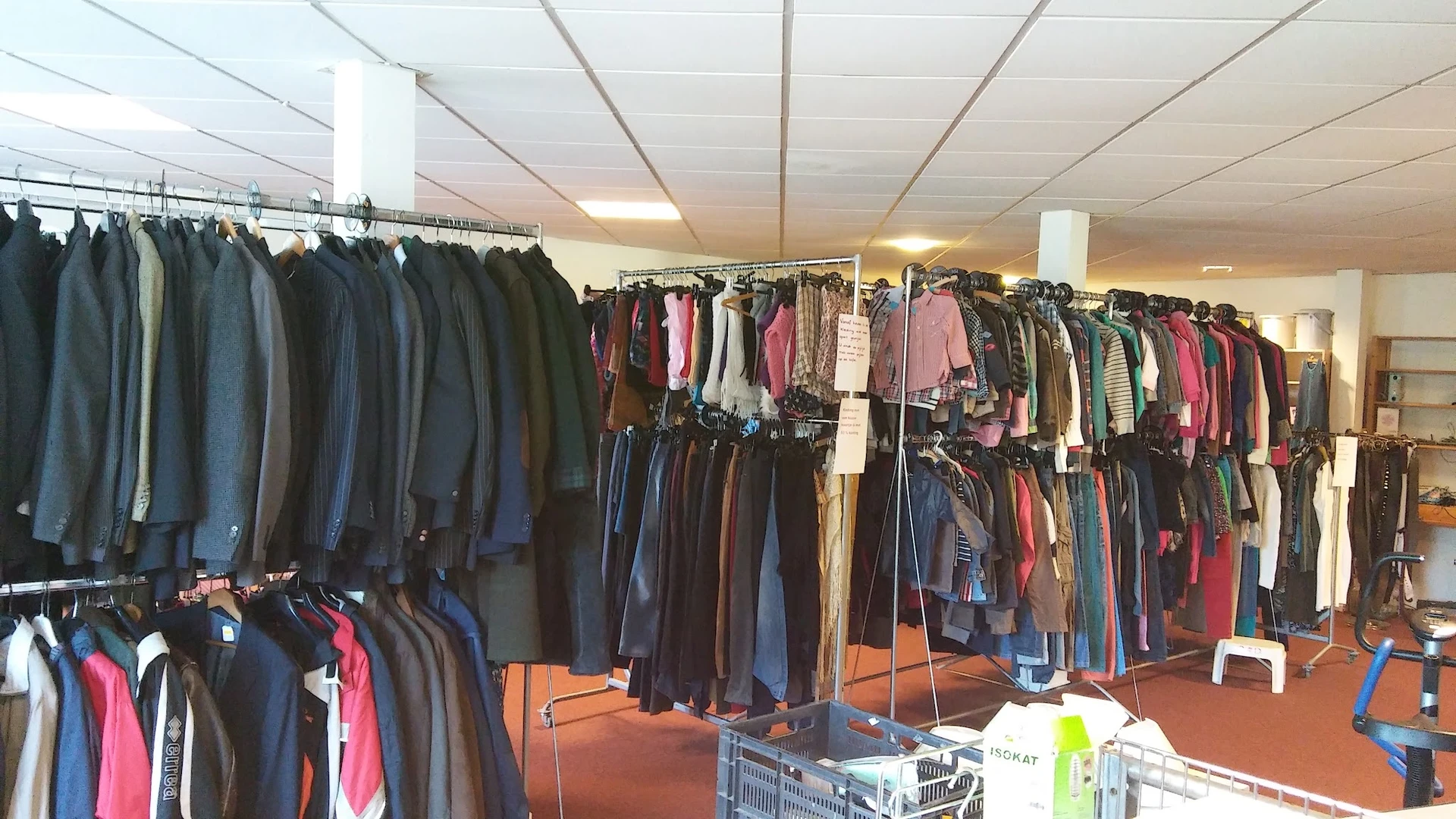Rekken met tweedehands kleding in verschillende kleuren en maten in de winkel