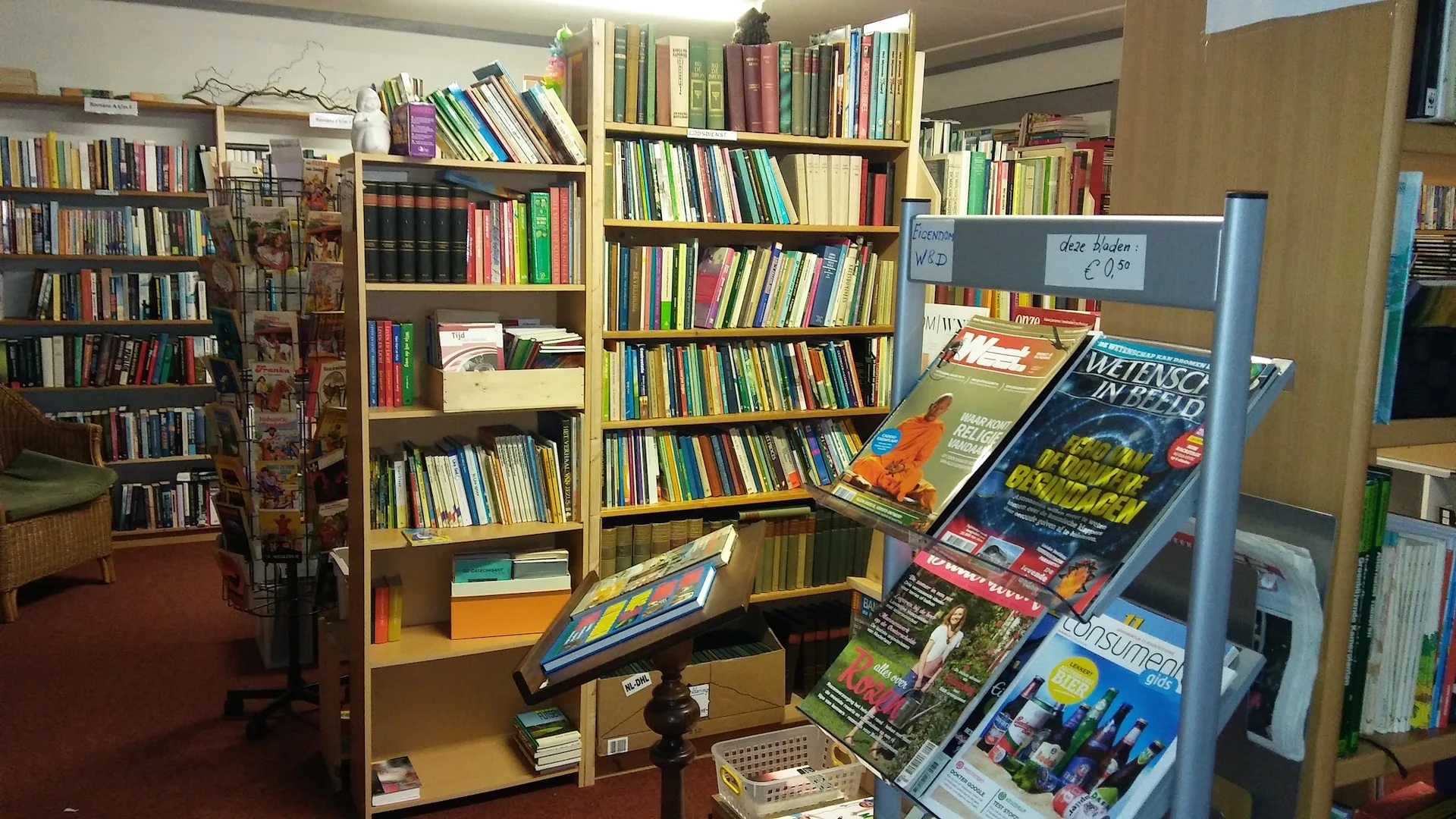 Boekenrekken met veel tweedehands boeken en een displayrek met dvd's en magazines op de winkelvloer