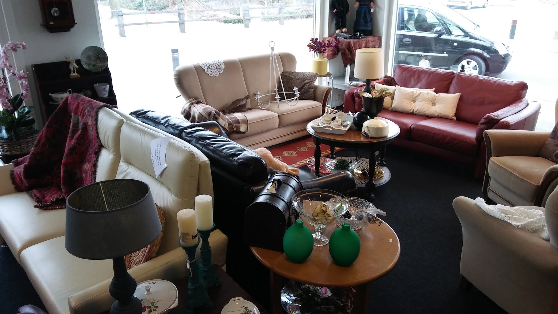 Showroom met diverse meubels: beige en rode banken, zwarte fauteuil, houten tafels, decoratie en verlichting
