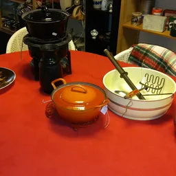 Rood tafelblad met huishoudelijke spullen: gouden pan met deksel, witte schalen en keukengereedschap