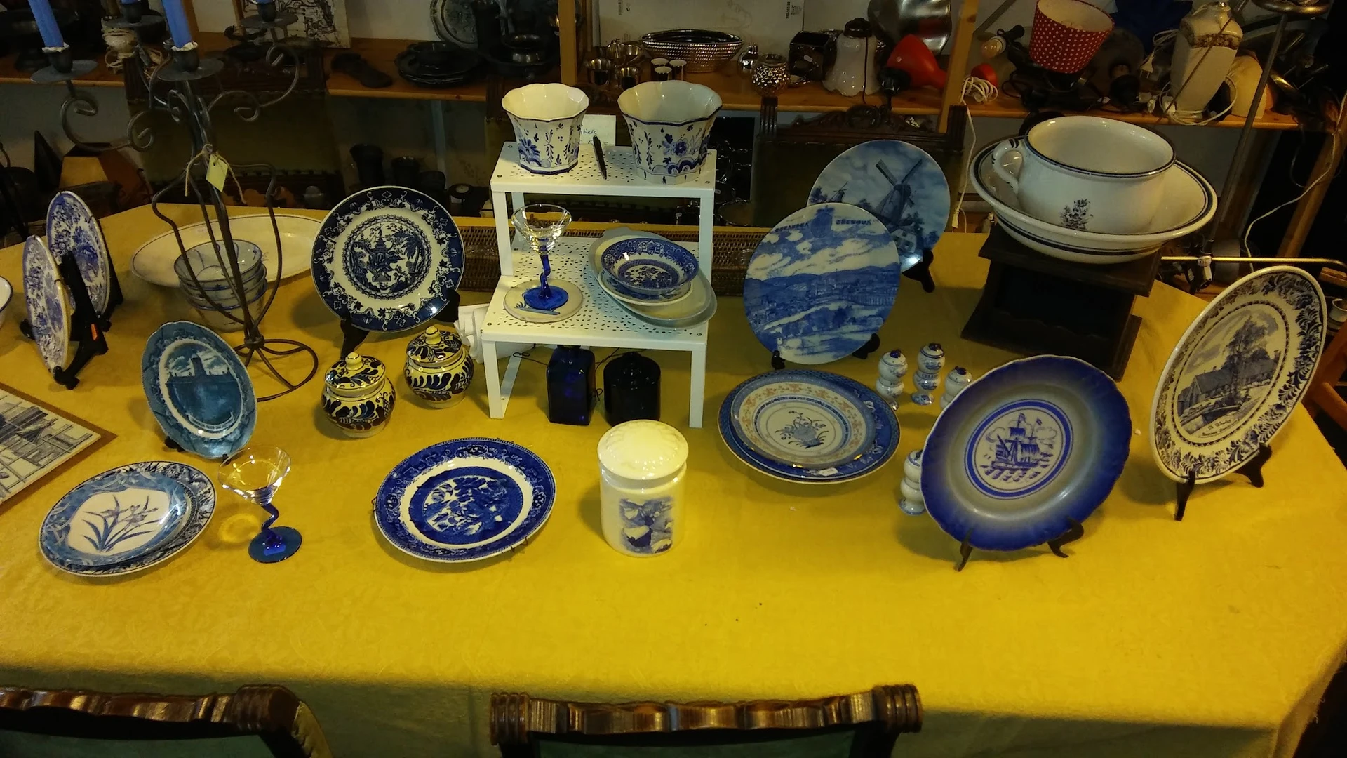 Uitstalling van blauw wit porselein servies, borden, kopjes en decoratieve items op gele tafel