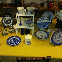 Uitstalling van blauw wit porselein servies, borden, kopjes en decoratieve items op gele tafel