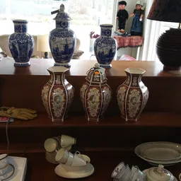 Houten kast met uitgestalde decoratieve vazen en serviesgoed, waaronder blauwe en wit porseleinen vazen en beige aardewerk.