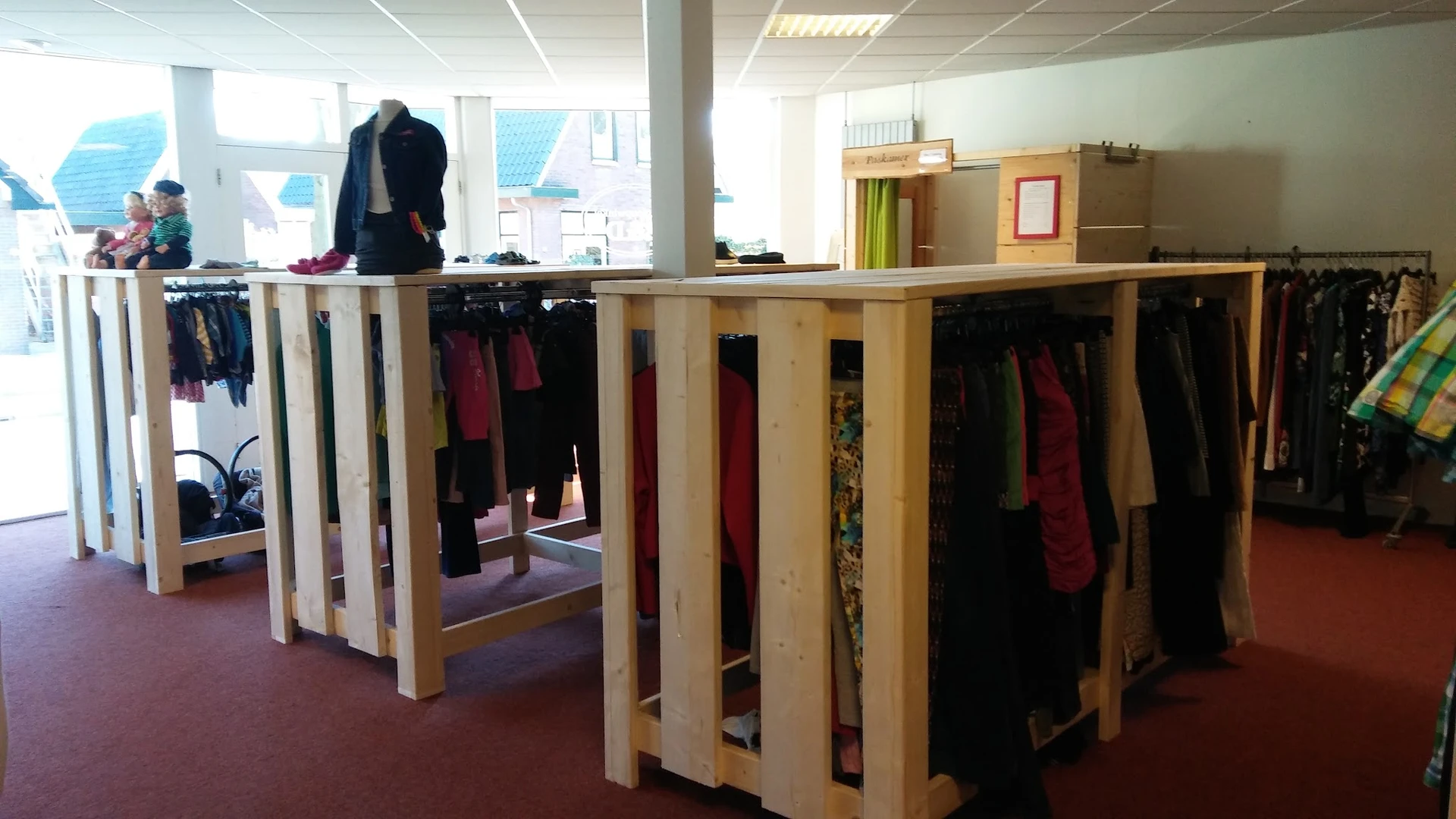 Houten kledingrekken met tweedehands dames- en herengkleding in verschillende kleuren