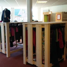 Houten kledingrekken met tweedehands dames- en herengkleding in verschillende kleuren