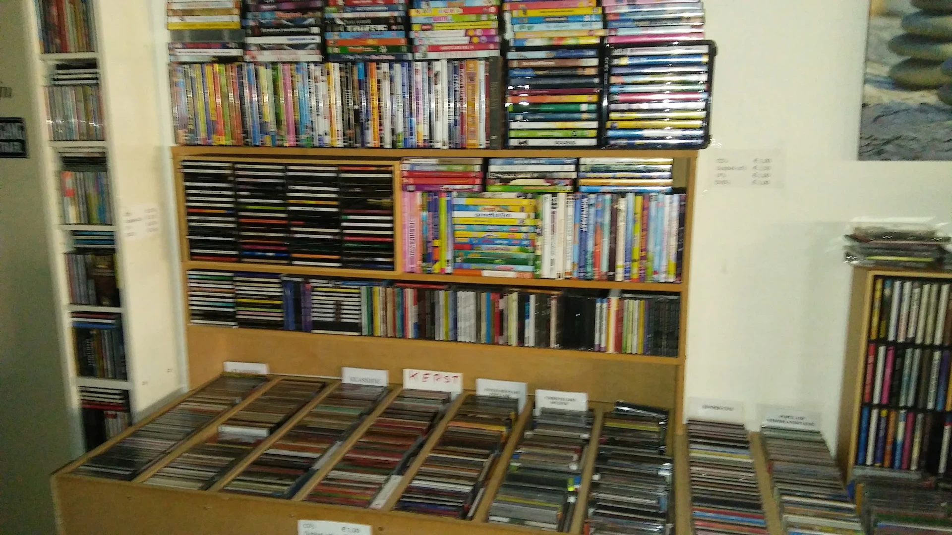 Uitgestalde cd's en dvd's in dozen op een tafel en in rekken tegen de muur.