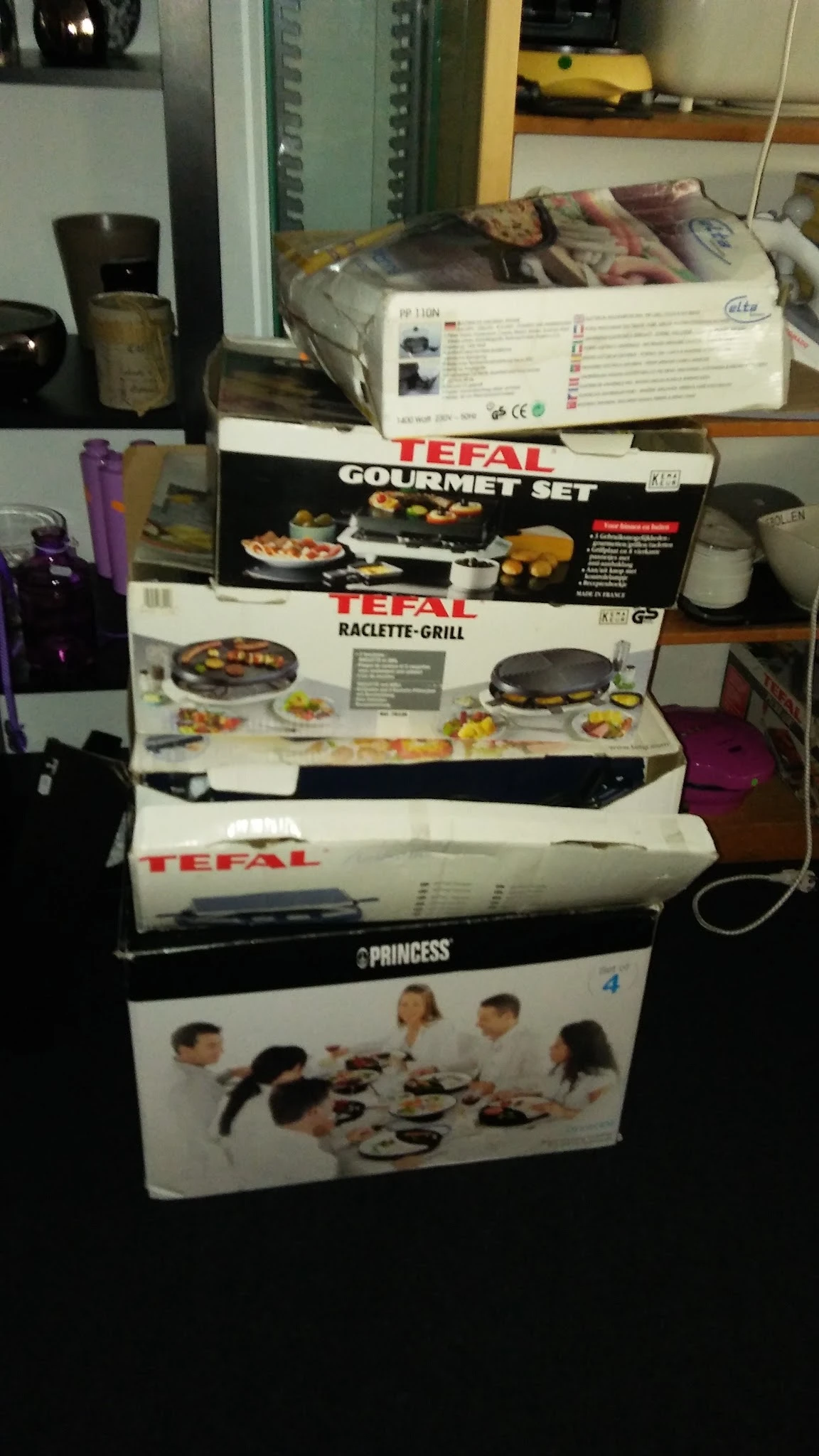 Gestapelde dozen met keukenapparatuur zoals Tefal gourmet set, raclette-grill en Princess producten