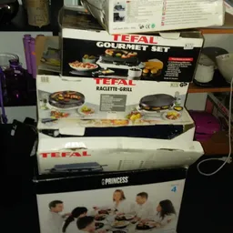 Gestapelde dozen met keukenapparatuur zoals Tefal gourmet set, raclette-grill en Princess producten