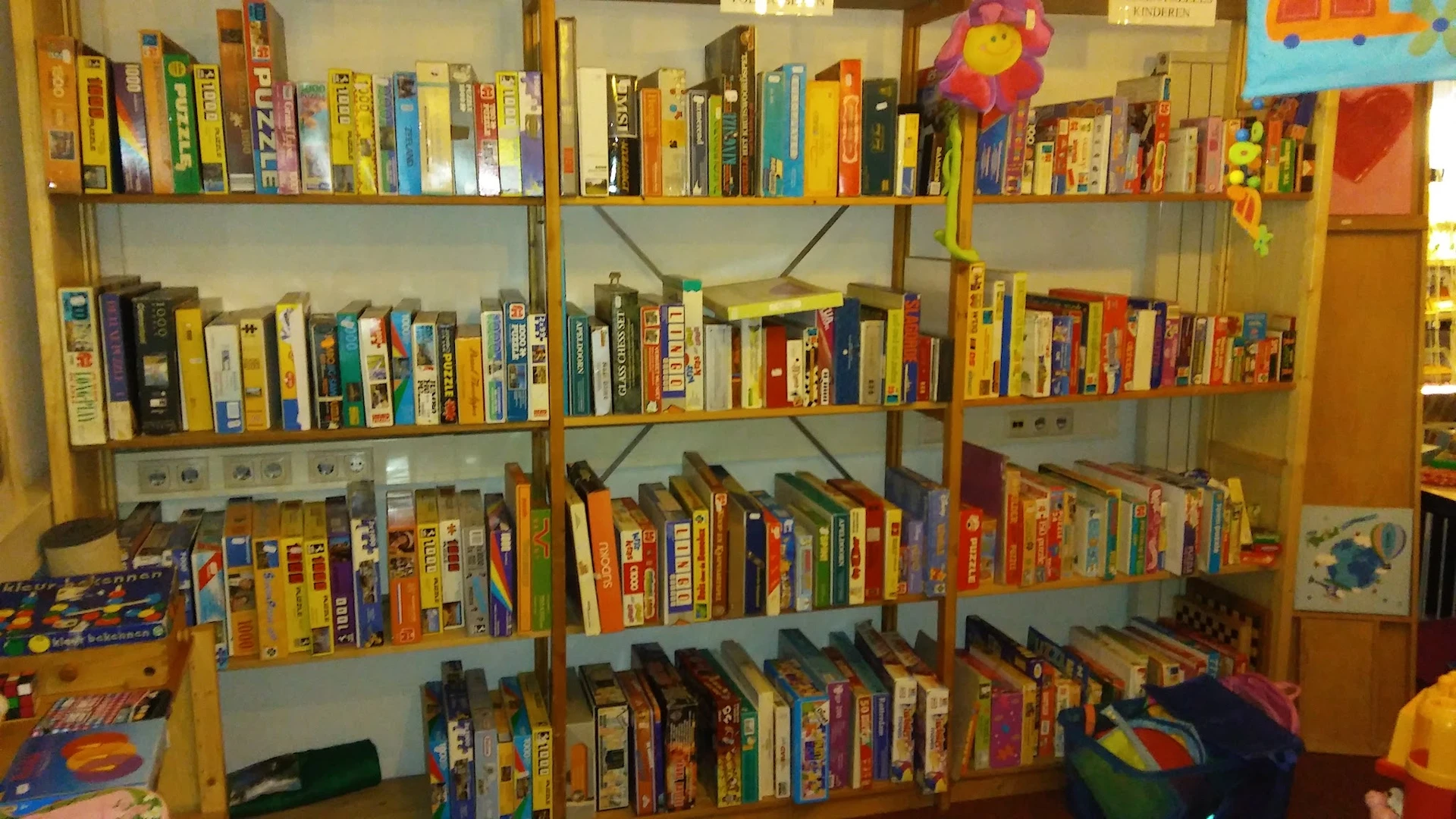 Houten stellingen vol met uitgekleurde bordspellen en gezelschapsspellen, netjes op alfabetische volgorde gerangschikt