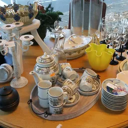 Uitstalling van wit en crème porseleinen serviesgoed, kopjes, schalen en theepot op houten tafel