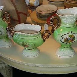 Groen servies met gouden handvatten en witte rand op een tafel, bestaande uit kommen en kannen