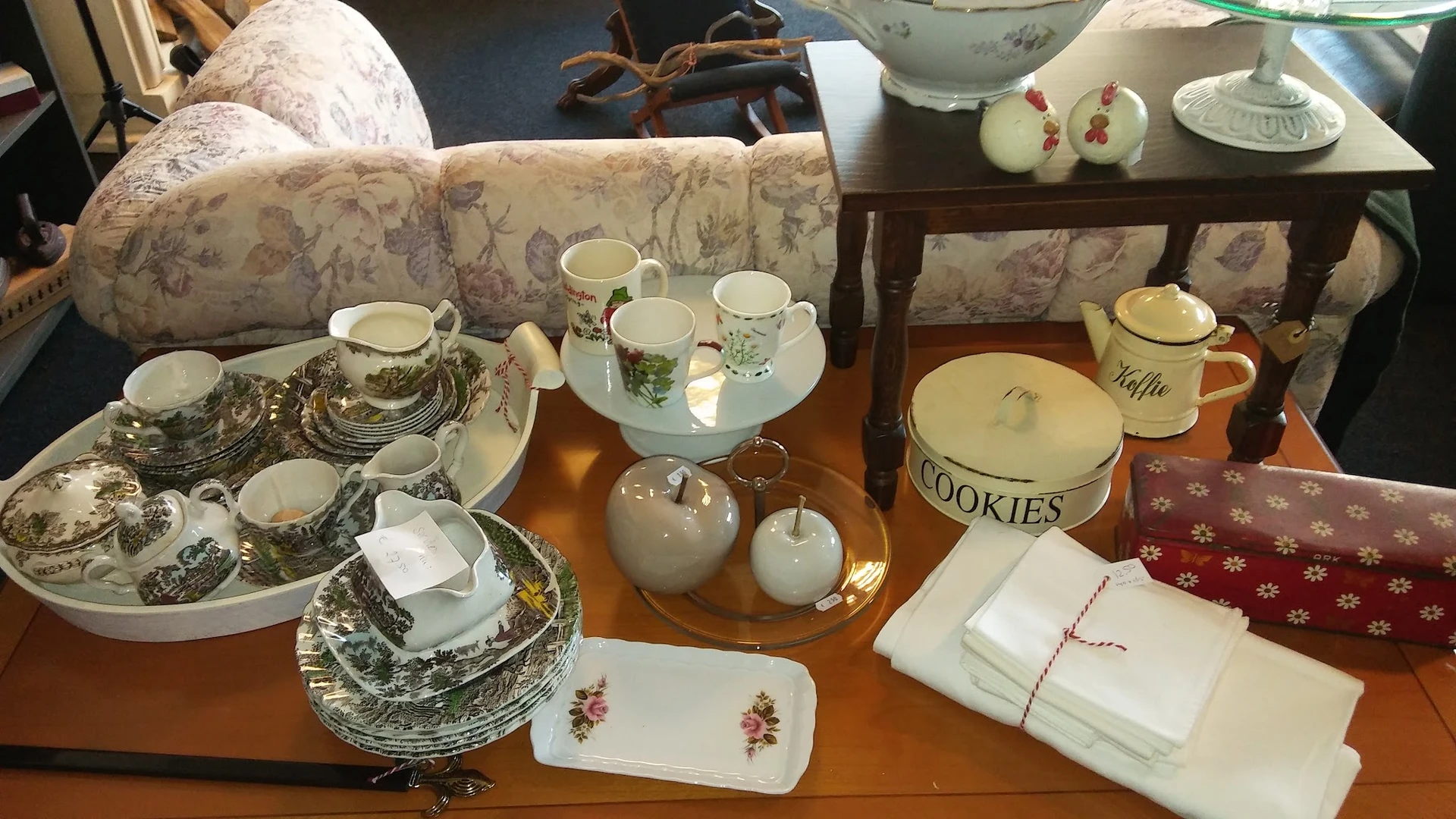Uitgestald servies en huishoudelijke artikelen op houten tafel, waaronder kopjes, borden, cookies-pot en decoratieve items