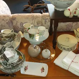 Uitgestald servies en huishoudelijke artikelen op houten tafel, waaronder kopjes, borden, cookies-pot en decoratieve items