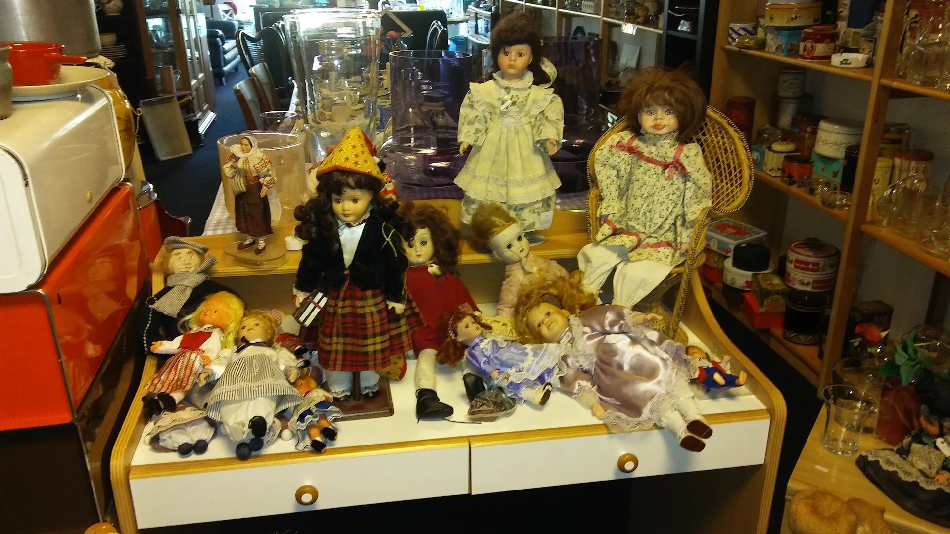 Verzameling antieke en vintage poppen in een vitrinekast, met verschillende kleertjes en accessoires uitgestald