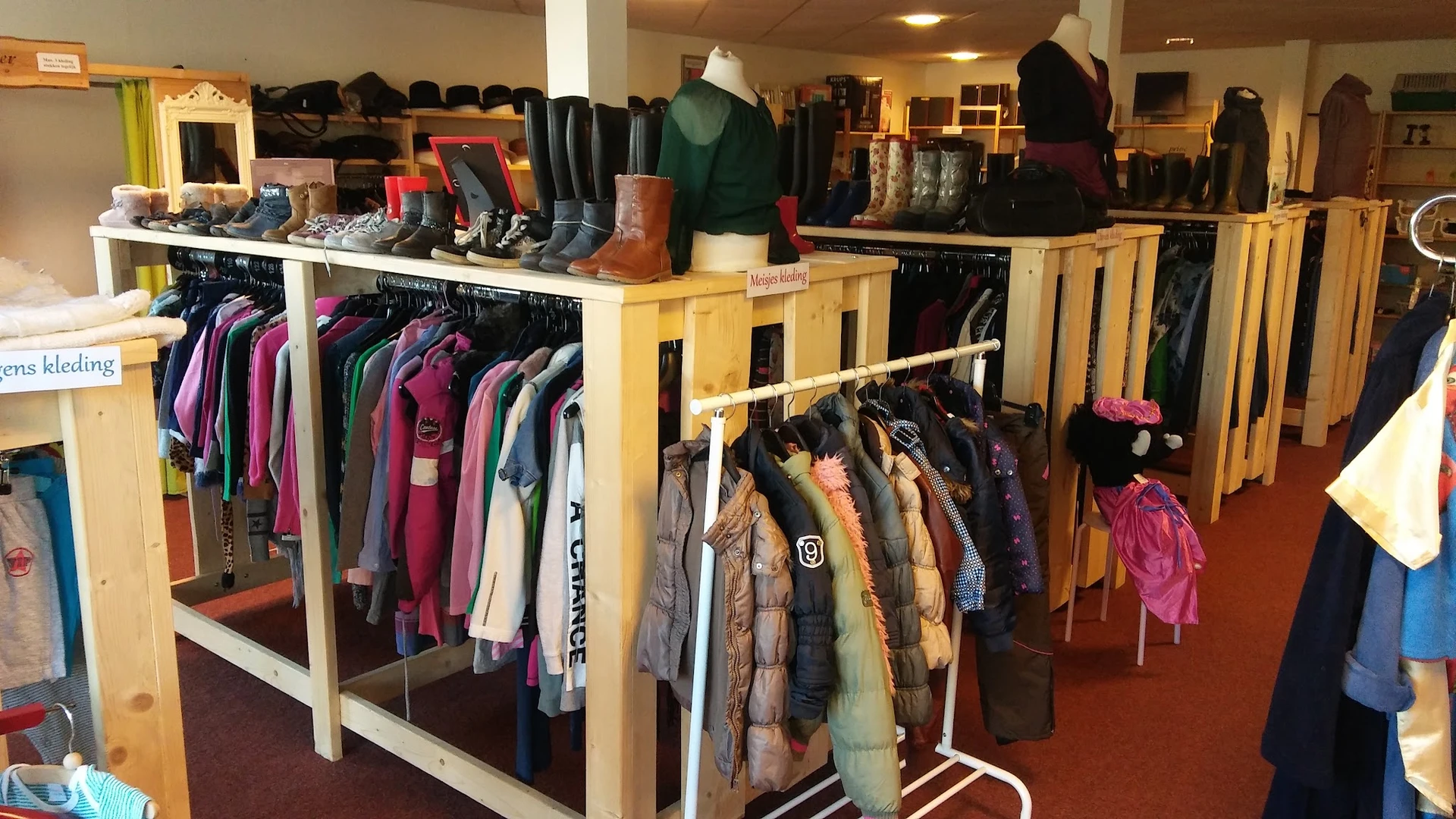 Rekken met tweedehands kleding, waaronder jassen, truien en jasjes in verschillende kleuren