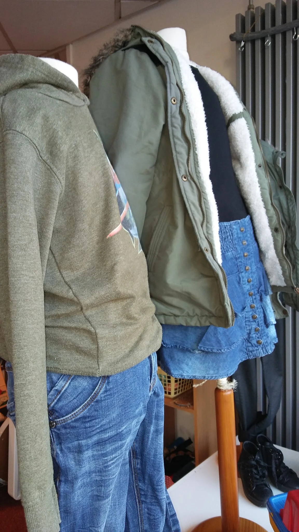 Tweedehands kleding op hangers: grijze sweater, olijfgroene jas met sherpa-voering en blauwe spijkerbroek