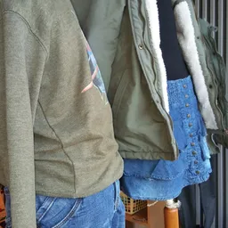 Tweedehands kleding op hangers: grijze sweater, olijfgroene jas met sherpa-voering en blauwe spijkerbroek