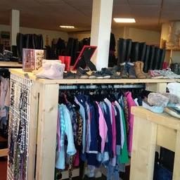 Rekken en toonbanken met tweedehands kleding, schoenen en accessoires in verschiedene kleuren