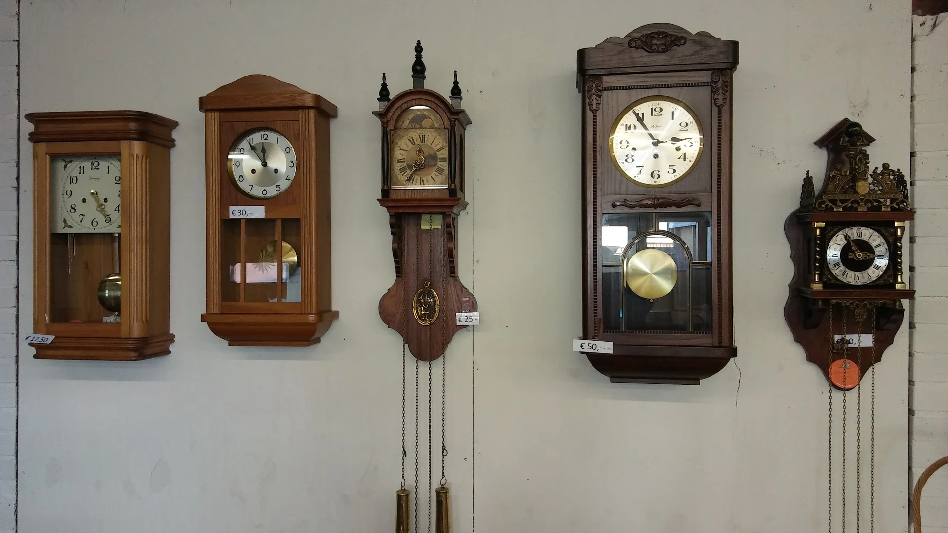 Vier houten wandklokken met verschillende stijlen en formaten tegen een witte muur