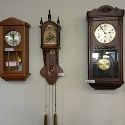 Vier houten wandklokken met verschillende stijlen en formaten tegen een witte muur