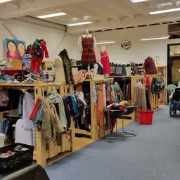 Winkelvloer met houten kledingrekken vol tweedehands kleding, mannequins met jurken, en winkelstellingen met diverse artikele