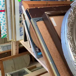 Verschillende spullen opgestapeld op een plank, waaronder frames, borden en huishoudelijke artikelen