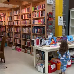 Binnenaanzicht van kringloopwinkel met grote boekenkast, werktafel en kind dat rondkijkt